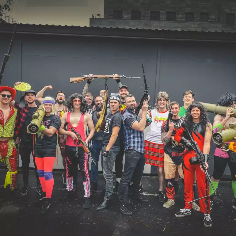 Large group on a bachelor party dressed in costumes visiting a gun range.