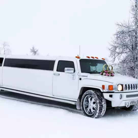 White hummer limo driving on a snowy road.