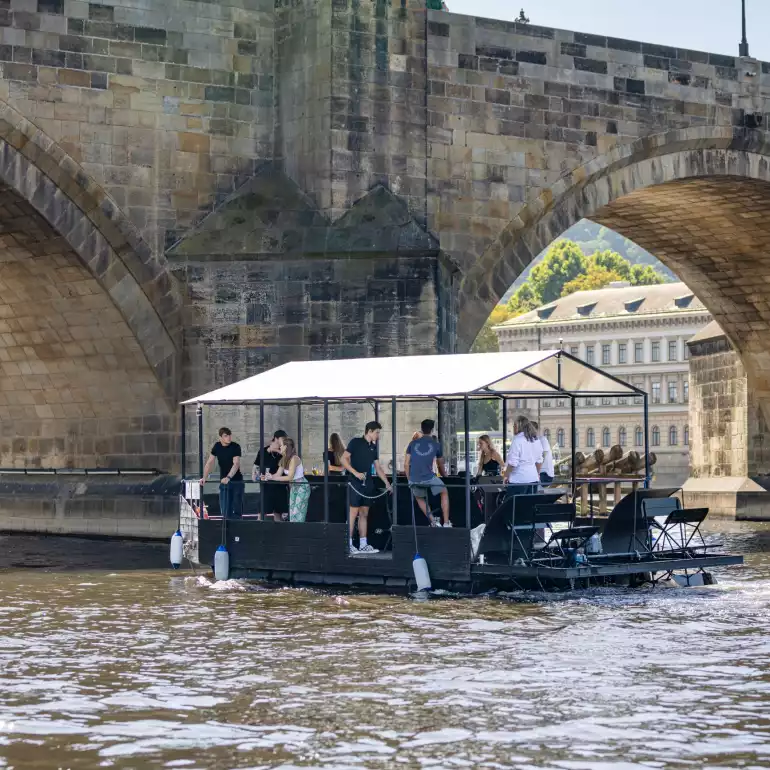 Prague party boat floating by a bridge on Vltava river.