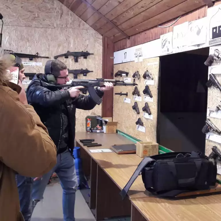 One man shooting an AK47 while being watched by an instructor in protective gear.