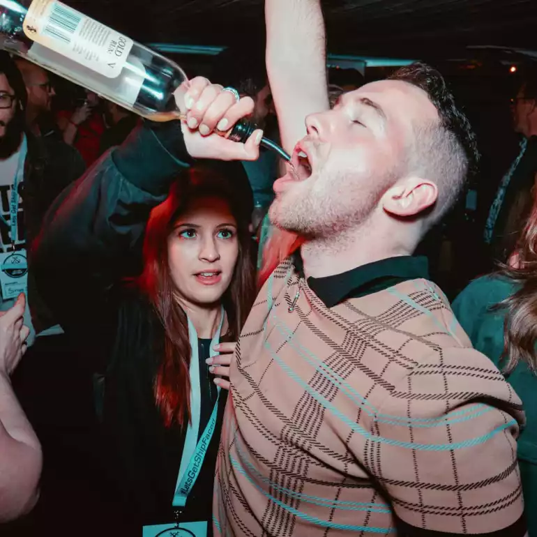 A girl serving a drink to a guy in a club straight from a bottle.