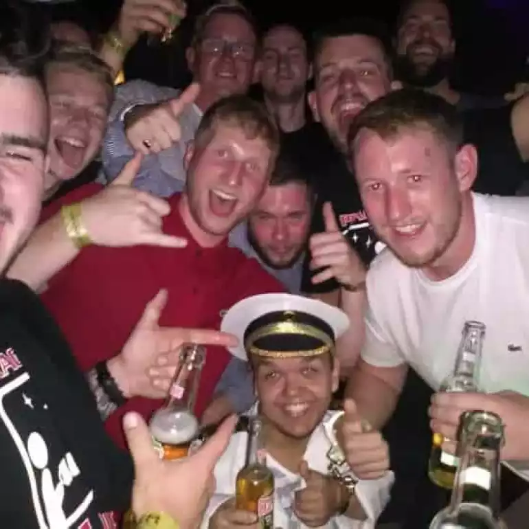 Large group of guys enjoying a welcome drink at a pub crawl with a dwarf entertainer.