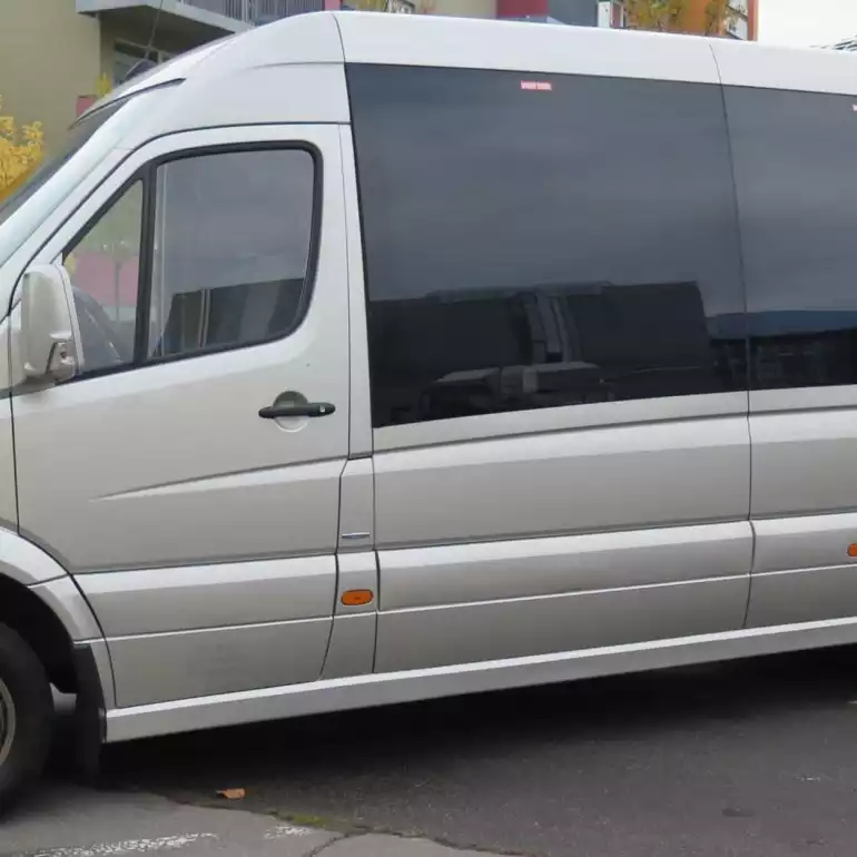 Large airport shuttle vain parked outside of a building.