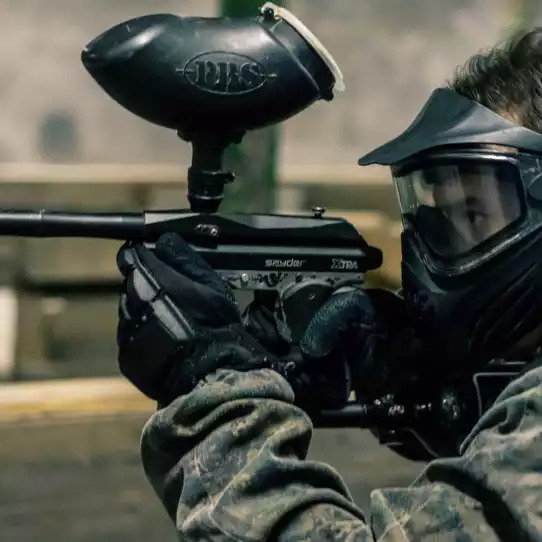 Paintball player in full gear with paintball gun and protective mask.