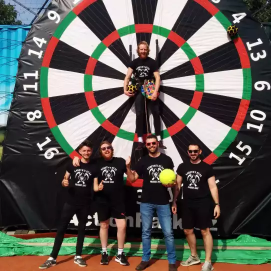 Four guys posing in front of a football darts target after pinning the groom to be in the middle of the target.