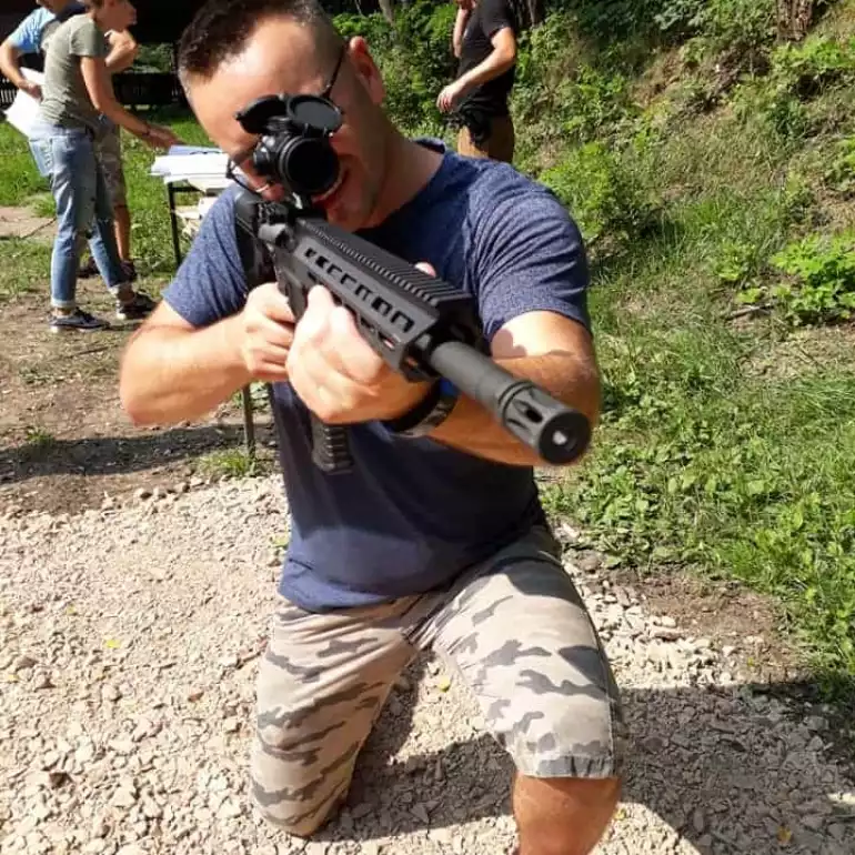 A guy on his knee aiming an AK47 at a gun range in Warsaw.