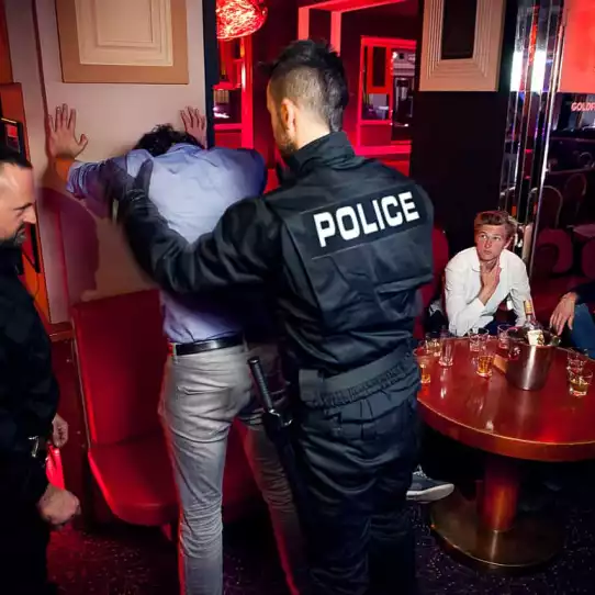 Group in a club watching a person standing agains a wall being searched during a bachelor party night.