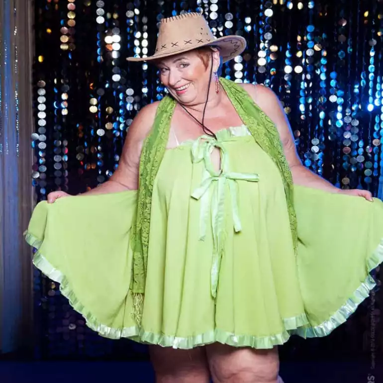 XXL strip show performer dressed in green dress wearing a hat.