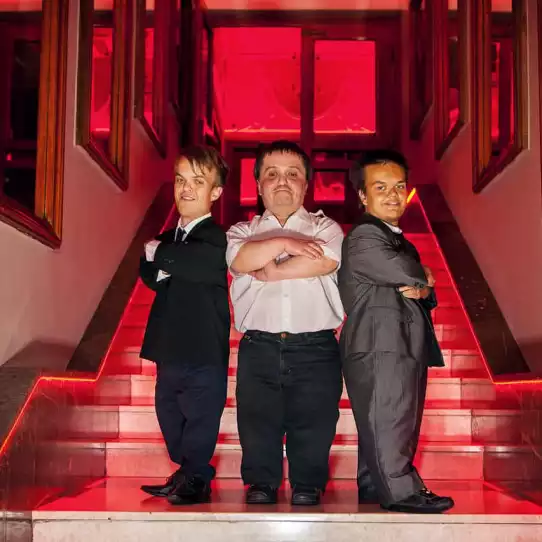 Three dwarf entertainers dressed up in suits standing on a staircase.